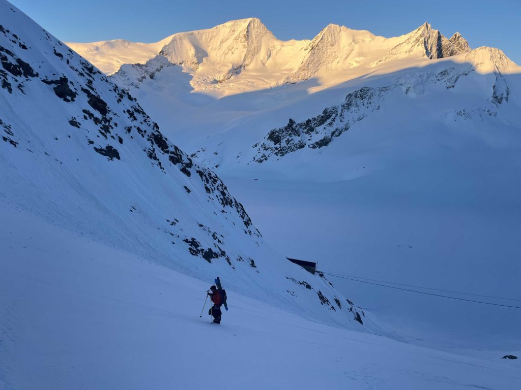 Homme remontant une pente avec skis sur le dos en direction du Finsteraarhorn. Lever de soleil en arrière-plan