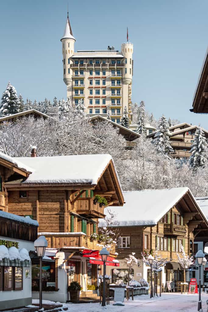 View of Gstaad Palace in winter with chalets below