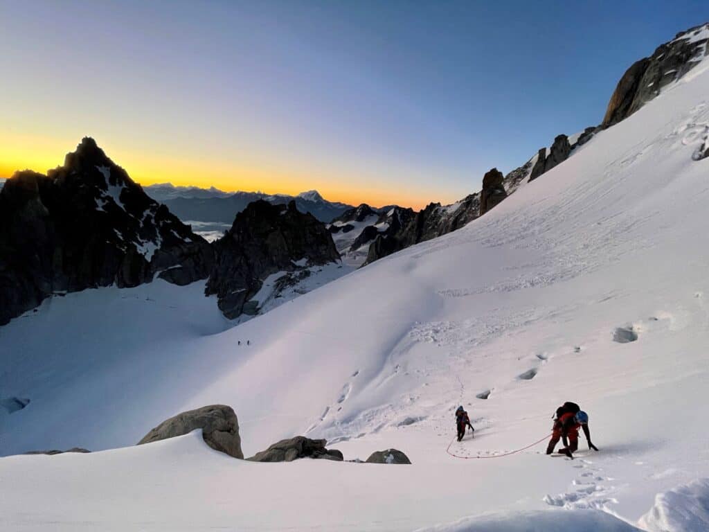 Guide de haute montagne encordé avec son client sur une pente de neige au lever du soleil