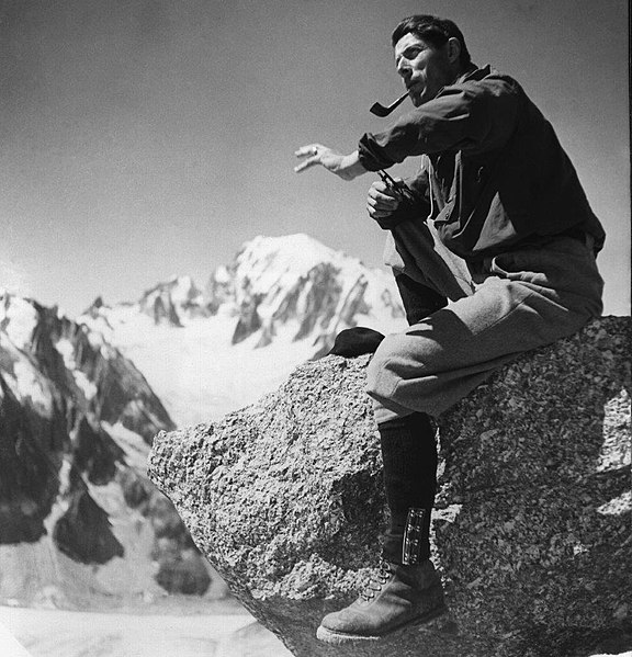 Alpiniste Roger Frison Roche sur un rocher, derrière lui, le massif du mont Blanc