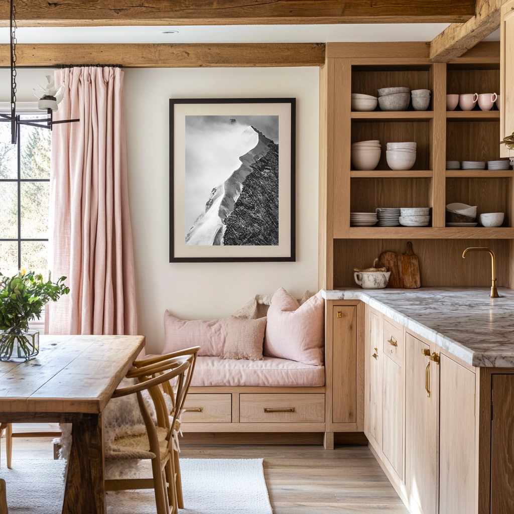 Cuisine en bois avec coin repas et photographie artistique de montagne – Une cuisine lumineuse et chaleureuse, avec des meubles en bois naturel et un plan de travail en marbre. Une photographie encadrée d’un sommet alpin émergeant de la brume apporte une touche artistique à l’espace. Le coin banquette avec coussins aux teintes douces et les étagères ouvertes créent une atmosphère conviviale et élégante, où la tradition alpine rencontre le raffinement contemporain.