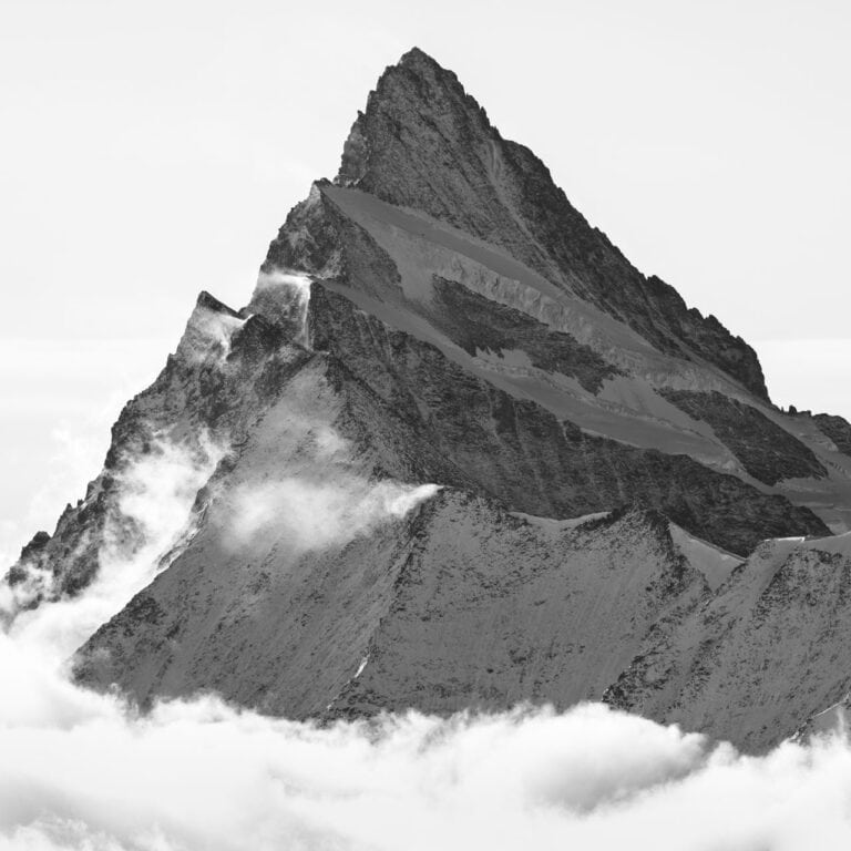 Schwarz-Weiß-Fotografie des Finsteraarhorns, einem Gipfel in den Berner Alpen, der mit seinem scharfen Grat und den Neuschneetexturen aus den Wolken auftaucht.