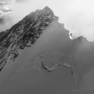 Schwarz-Weiß-Fotografie des Nordend (4608 m) mit beleuchtetem Zinnengrat, umgeben von Dunst und Wolken in den Schweizer und italienischen Alpen.