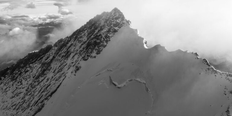 Photographie noir et blanc du Nordend (4608 m) avec arête crénelée éclairée, entourée de brume et de nuages dans les Alpes suisses et italiennes.