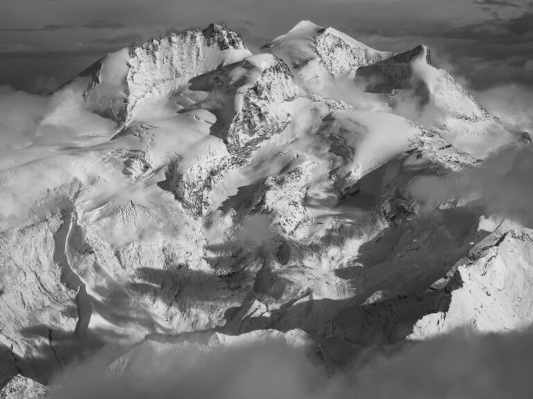 Photographie noir et blanc du Strahlhorn et du Rimpfischhorn après les premières neiges d'automne, révélant glaciers et reliefs dans les Alpes valaisannes.